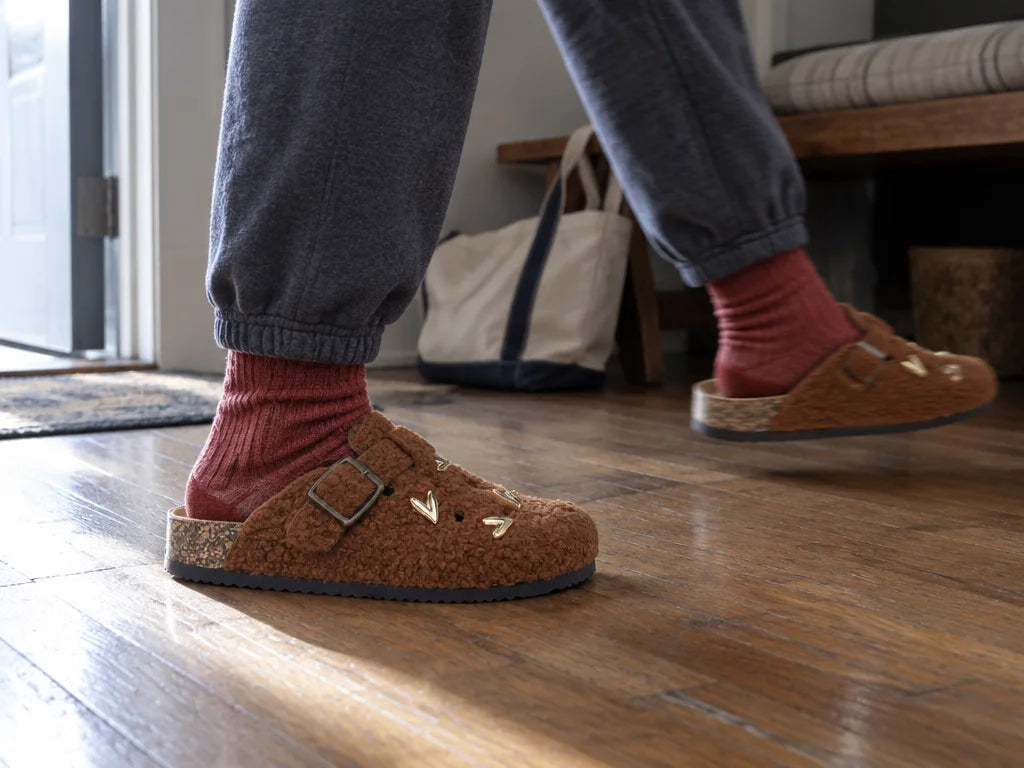 A 4:3 photograph of the exact caramel teddy-wool BIRKROCS mule from reference r13 worn as a real pai